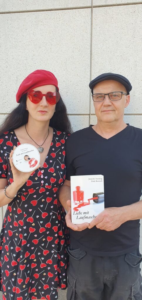 Auf dem Bild sind zwei Personen zu sehen, eine Frau und ein Mann. Die Frau trägt ein schwarzes Kleid mit roten Herzmotiven, eine rote Baskenmütze und eine rote herzförmige Sonnenbrille. Sie hält eine CD in der Hand, auf der "Liebe mit Laufmaschen" steht. Der Mann trägt ein schwarzes T-Shirt und eine schwarze Schirmmütze. Er hält ein Buch mit dem Titel "Liebe mit Laufmaschen" in der Hand. Beide stehen vor einer hellen Wand. (Bildbeschreibung von Be My AI)